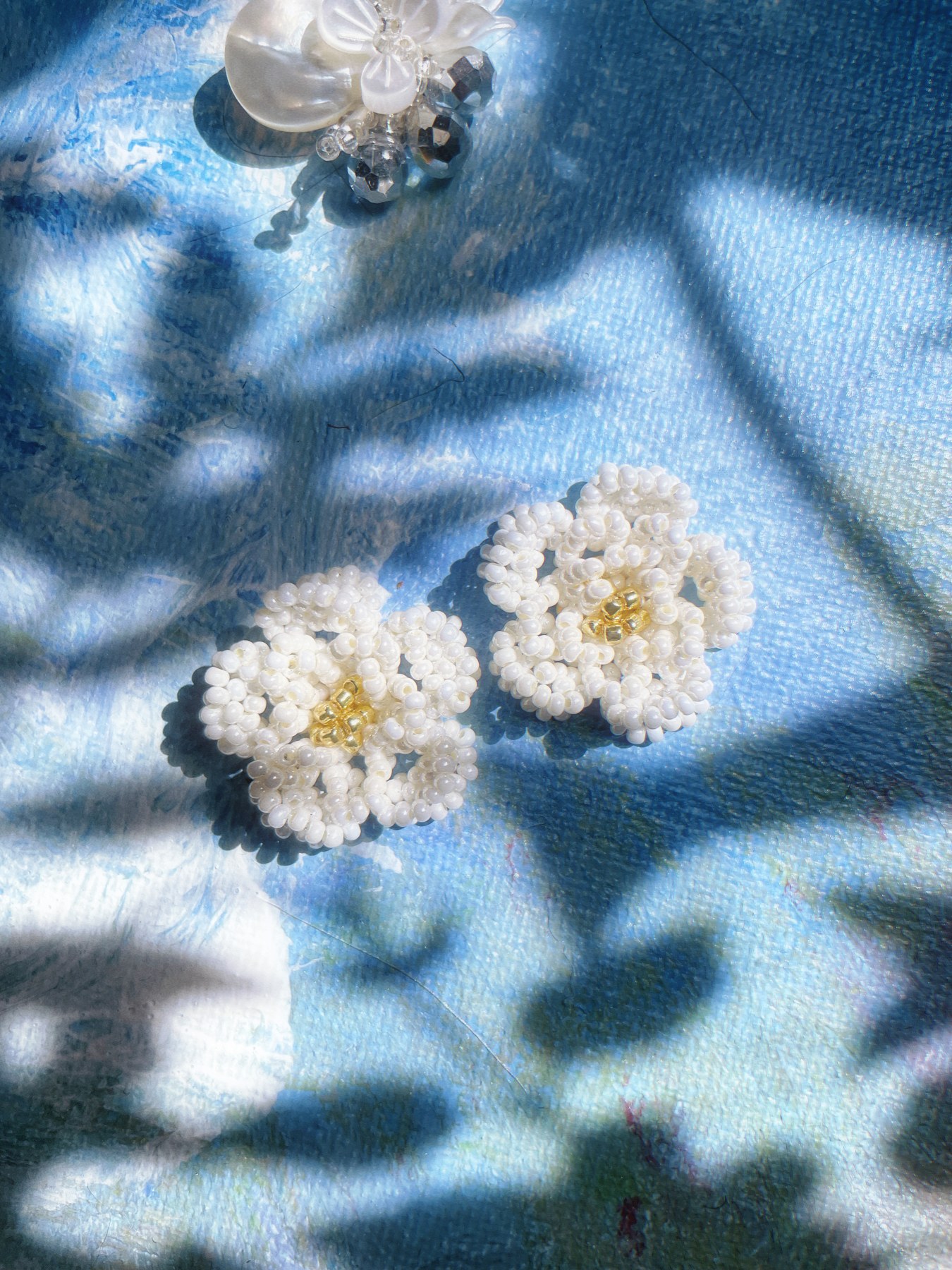 White daisy earrings against a blue background